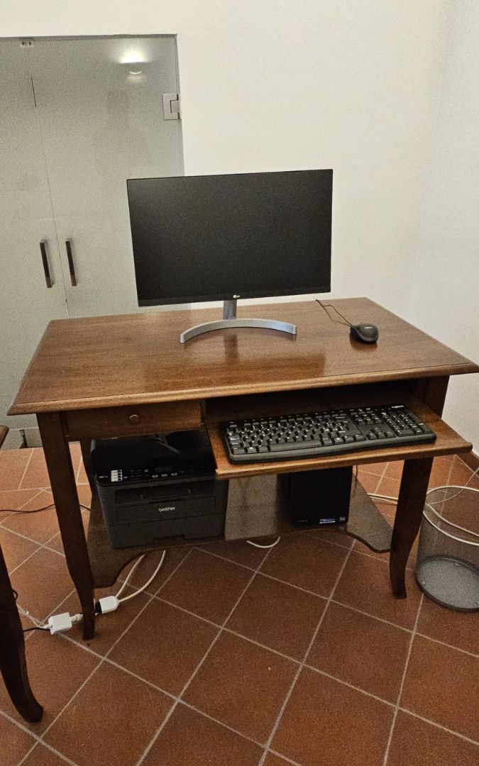 Scrivania classica in legno color noce scuro con monitor PC, tastiera e stampante posizionata su ripiano inferiore.